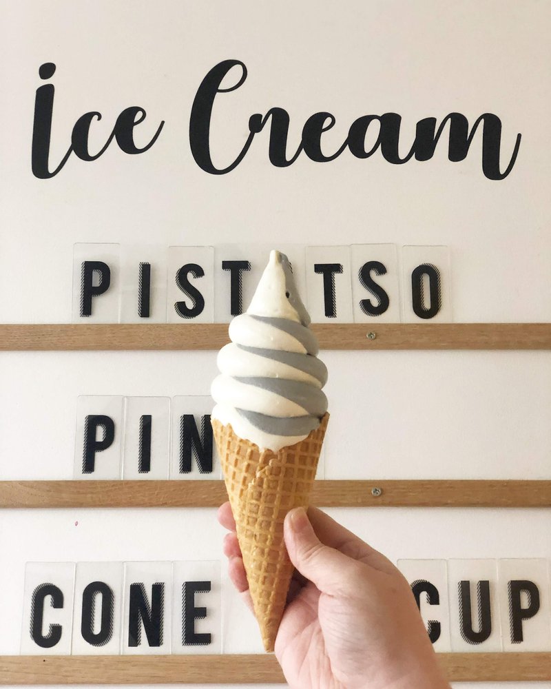 A hand holds an ice cream cone in front of a sign