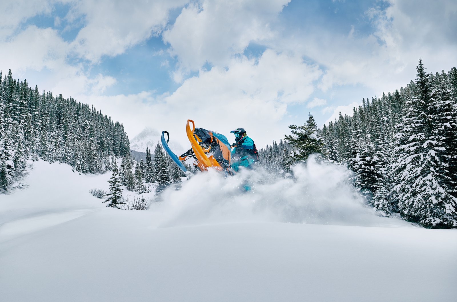 A snowmobiler driving through deep powdery snow in Crowsnest Pass, surrounded by snow-covered evergreens.