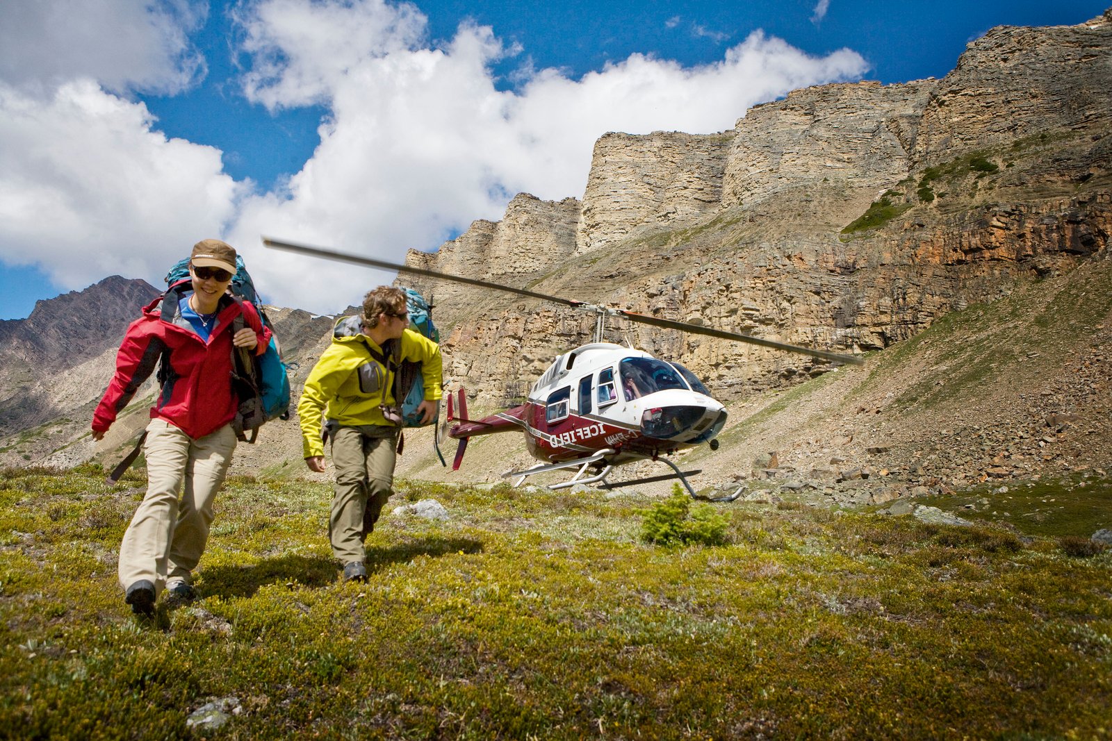 Two people crouched as they walk away from a running helicopter that landed in the alpine of the mountains.