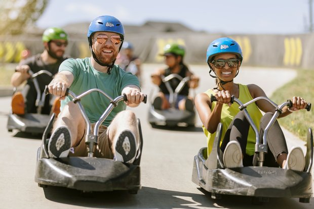 A group of people smiling while they go downhill karting at an outdoor track.