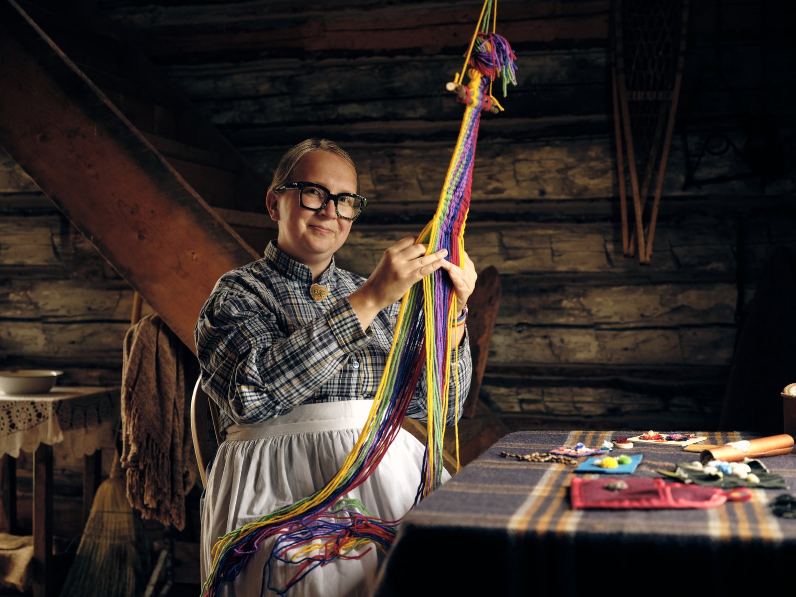 Indigenous women smiling at the camera while sitting and making Indigenous art with colourful string.