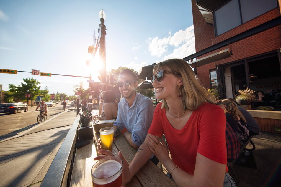 Couple having a beer on a sunny patio overlooking a street.