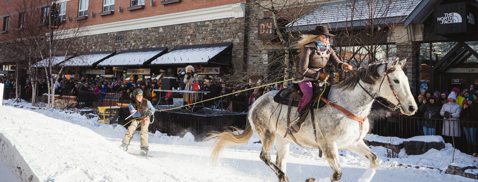 Spectators line the street while enjoying a skijoring event during a winter festival.