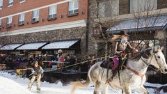 Spectators line the street while enjoying a skijoring event during a winter festival.