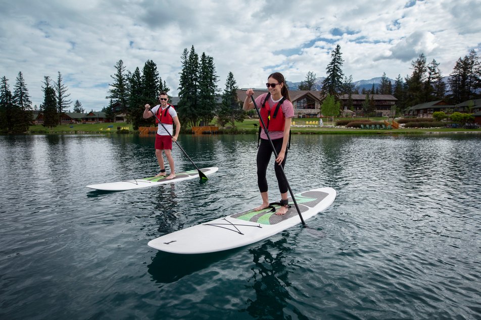 A couple of paddleboarders paddle on Lac Beauvert with the Jasper Park Lodge in the background.