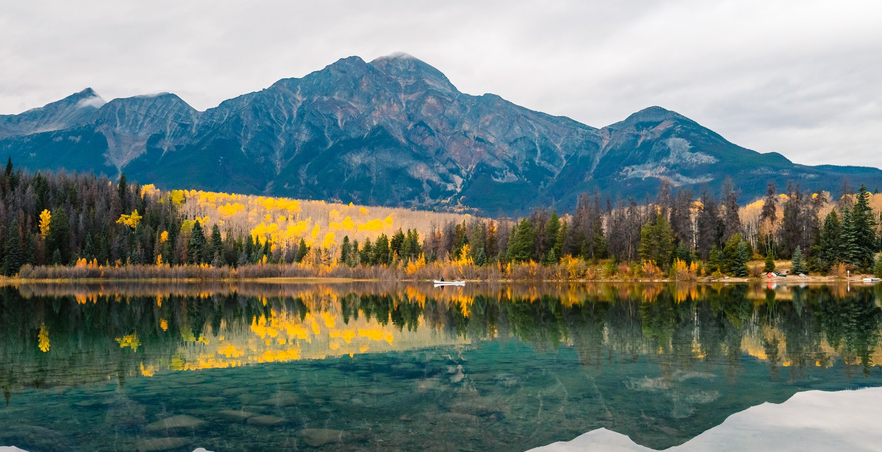 Two people in a white canoe paddle on Patricia Lake in Jasper National Park, with mountains in the background.