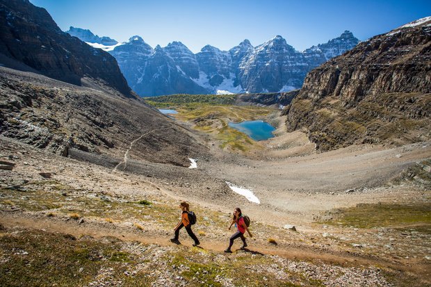 Two hikers hiking through an alpine valley on a summer day with mountain view in the background