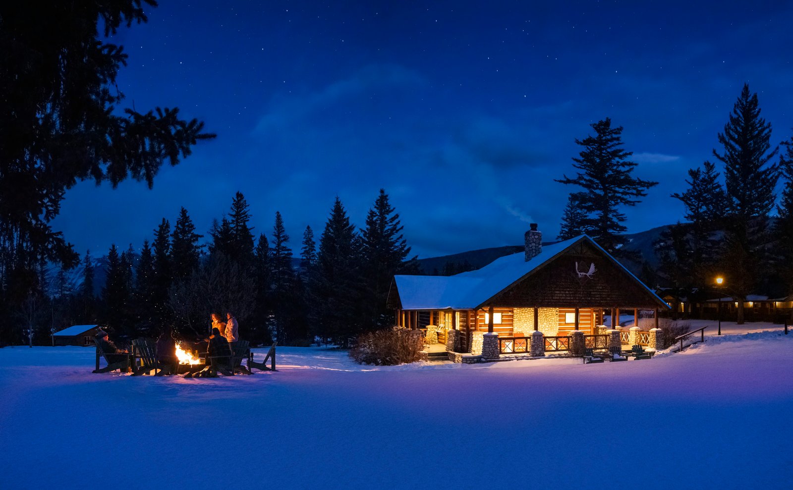 Group around a fire in front of a lodge during a winter night.