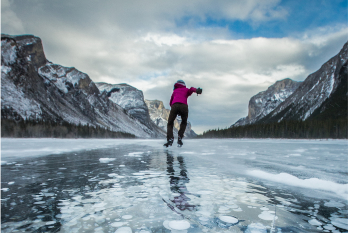 A lone person ice skates on the ice bubbles created under the water from a frozen lake.