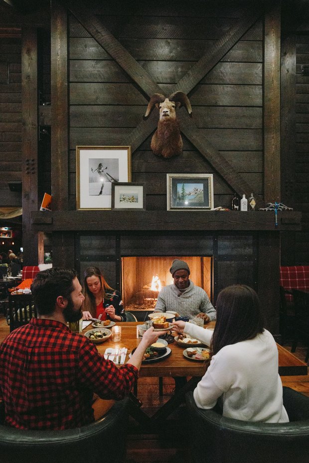 Friends sitting around the dinner table in front of a fireplace at Park Distillery in Banff
