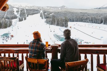 A couple has a drink on a patio overlooking the ski resort after a day of skiing at Lake Louise Ski Resort in Banff National Park.