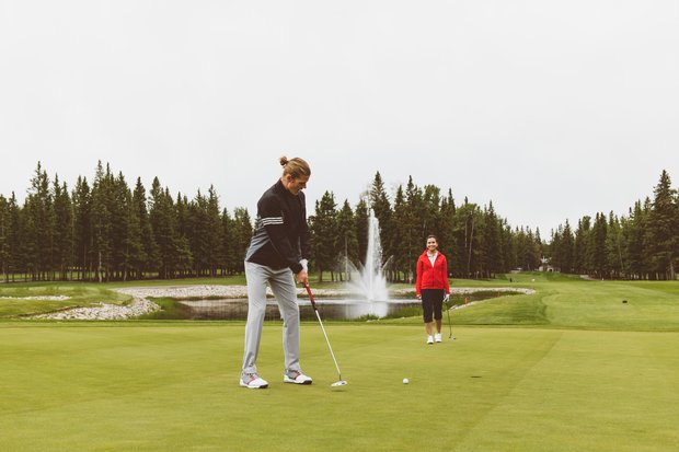 A couple golfing at the Sundre Golf Club and the man is putting on the green.