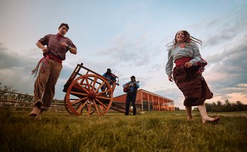 traditional dancers and musicians at Metis crossing perform in front of a wooden cart.