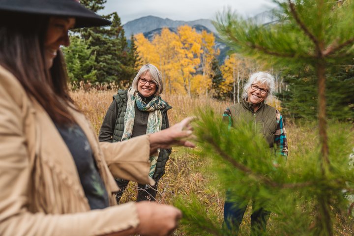 Two elderly women smiling as they listen to an Indigenous guide talking about the tree they are pointing at.