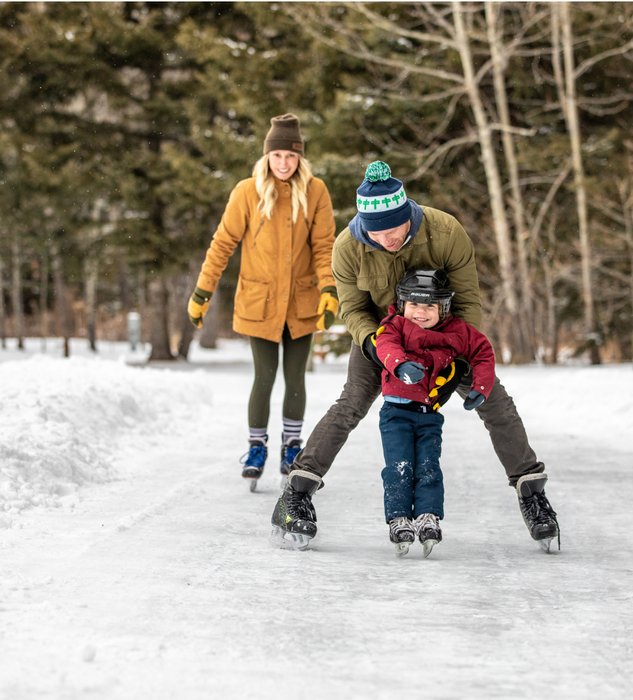 Two parents and their child smiling while they skate on an ice pathway.
