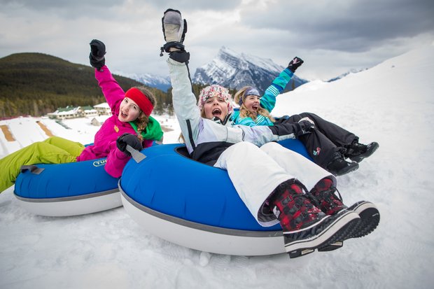 A group of children at the top of a tube run with smiles and their hands in the air before taking the ride down.