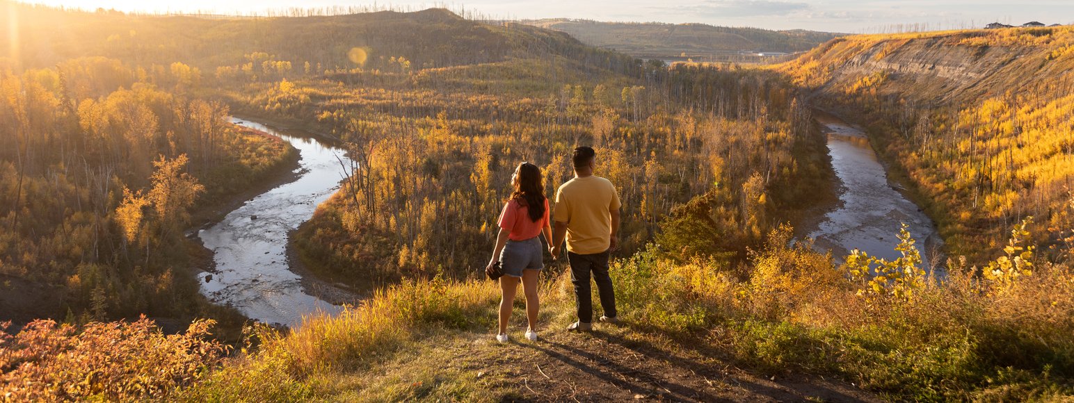 Two people looking over river lookout and the autumn trees during a sunset.