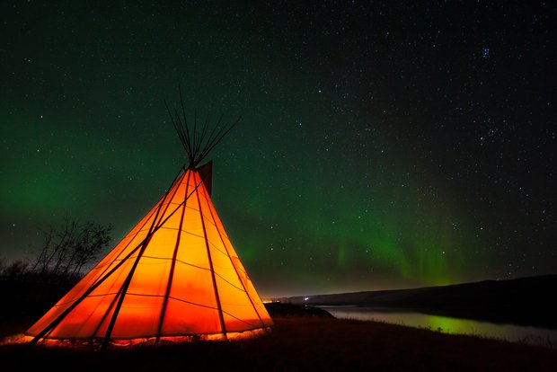 An orange teepee in rural Alberta with Northern Lights in the sky.