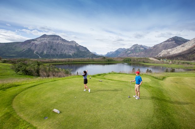 Couple golfing at Waterton Lakes Golf Course with the mountains in the background.