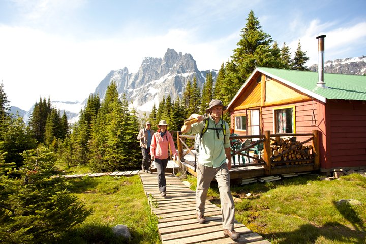 Three people carrying fishing rods walking on a boardwalk by the Tonquin Valley Backcountry Lodge in Jasper National Park, Alberta