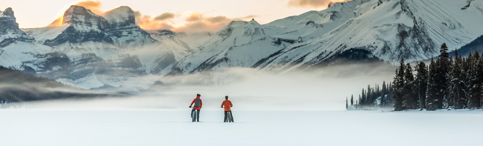 Two people fat biking on Maligne Lake with mountains in background