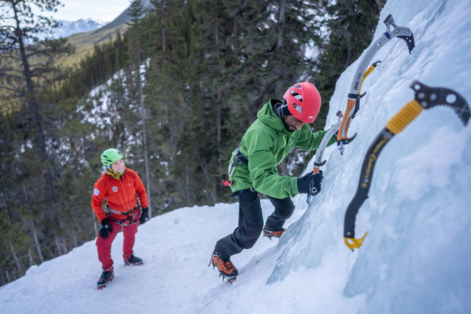 Two climbers using their gear and ice picks on an ice wall while ice climbing.