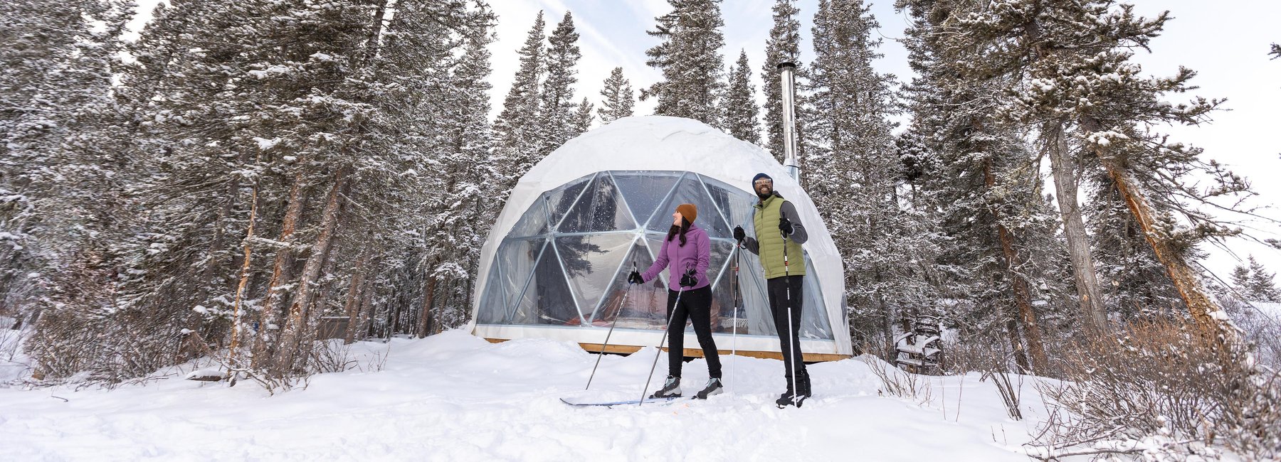 Couple skiing outside in front of dome tent with Elevated Escapes