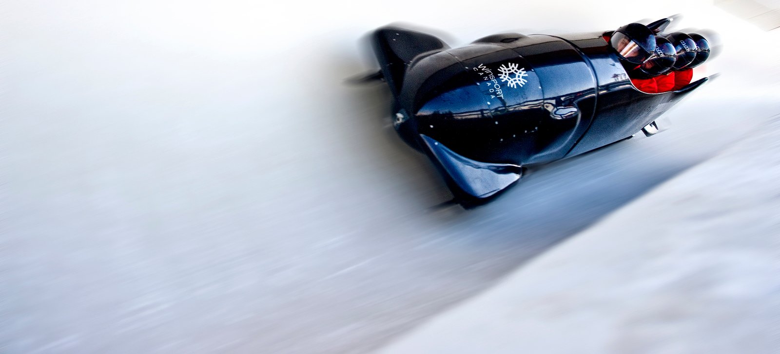 Blurry bobsled as it rides past the camera with four people in it.