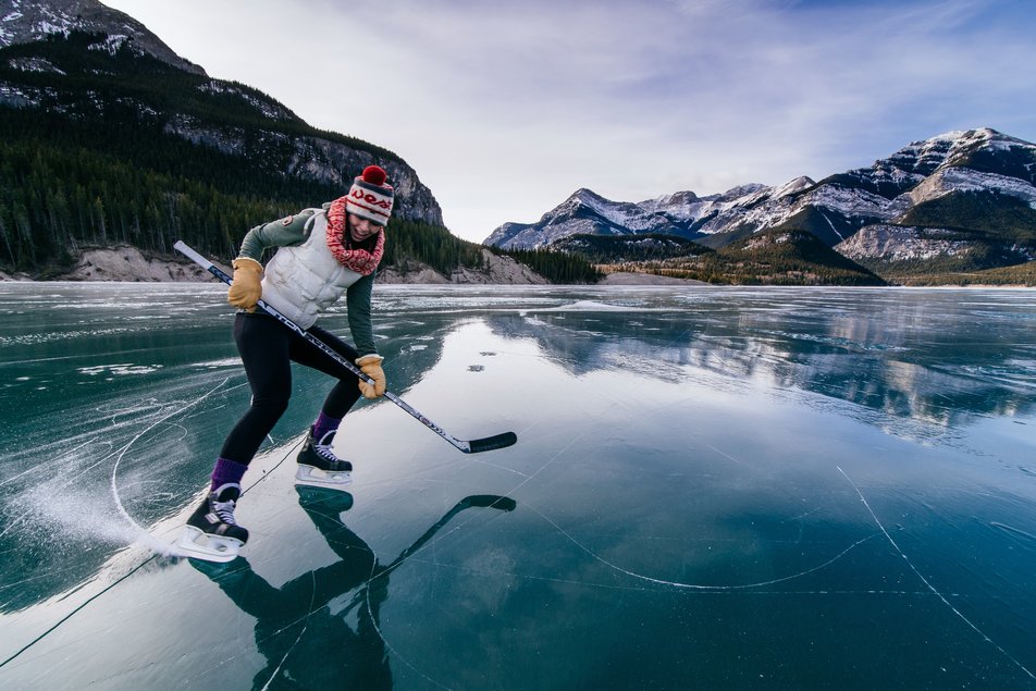 Player holds hockey stick while playing pond hockey on a glass-looking frozen lake.