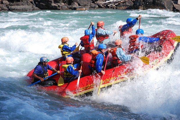 Group getting splashed by water as the whitewater rafting boat rides into a wave.