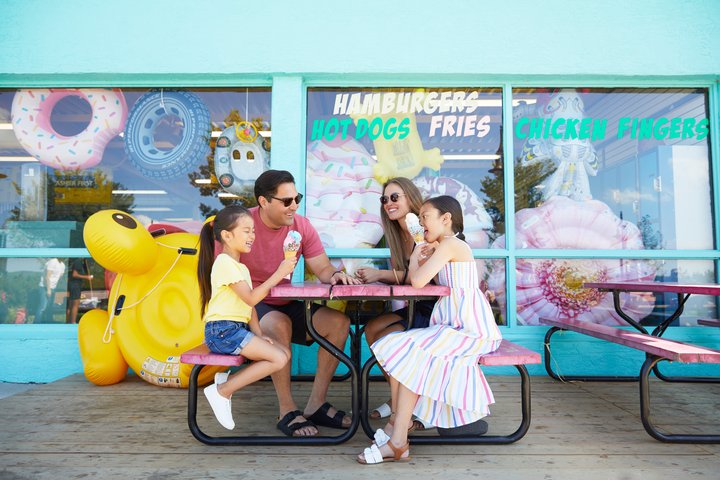 A family enjoying ice cream cones on a summer day sitting at a picnic table outside of the More Moo ice cream shop.