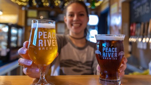Woman holding two beverages inside of the Peace River Brewing brewery.
