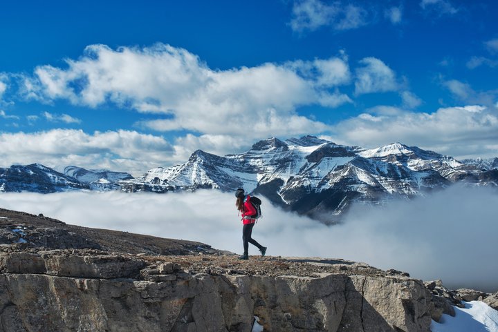 Woman hiking on a cliff with snow-capped mountain peaks in the background.
