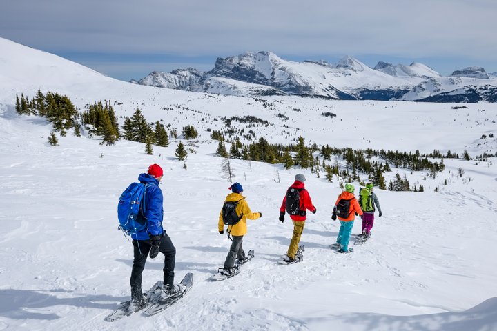 Group of five snowshoeing through a snow packed mountain valley.