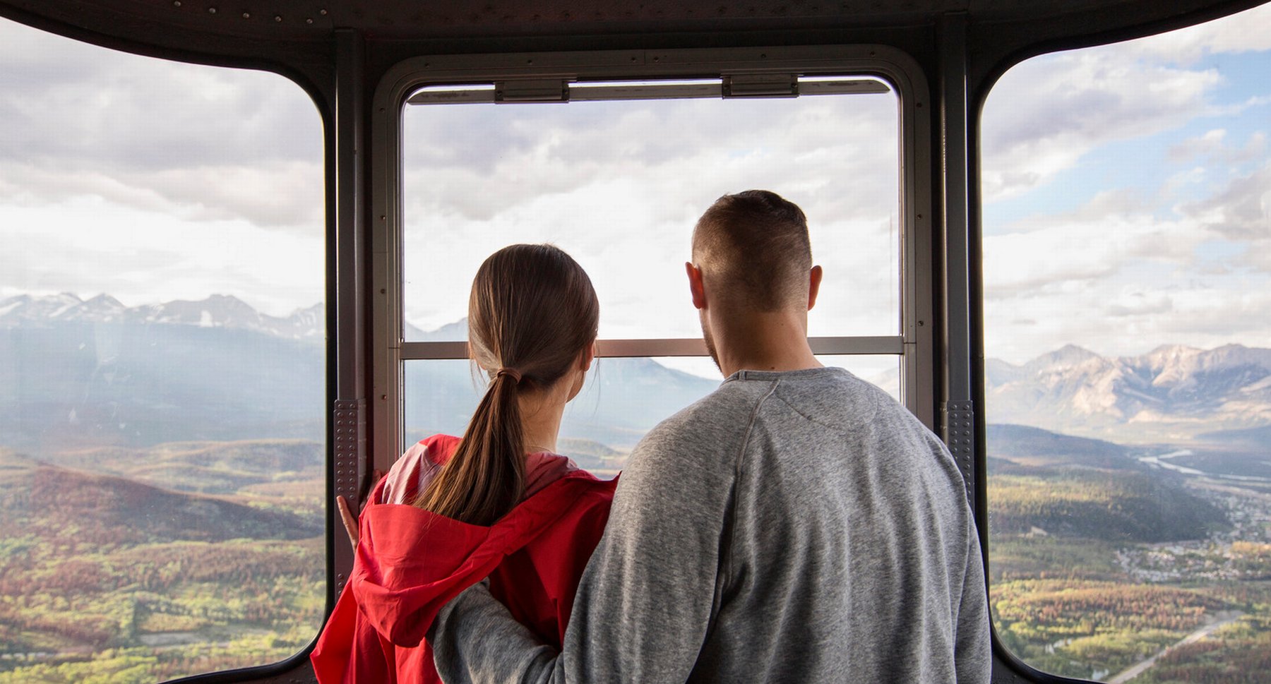 Couple look out of the jasper sky tram gondola window onto the mountain valley of Jasper National Park.