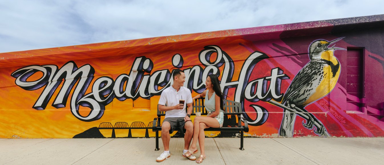 Couple sitting on bench with a mural behind them in downtown Medicine Hat.