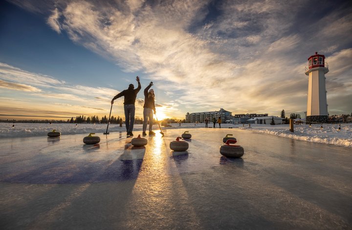 People curling on Sylvan Lake under wide-open skies and in front of a lighthouse.